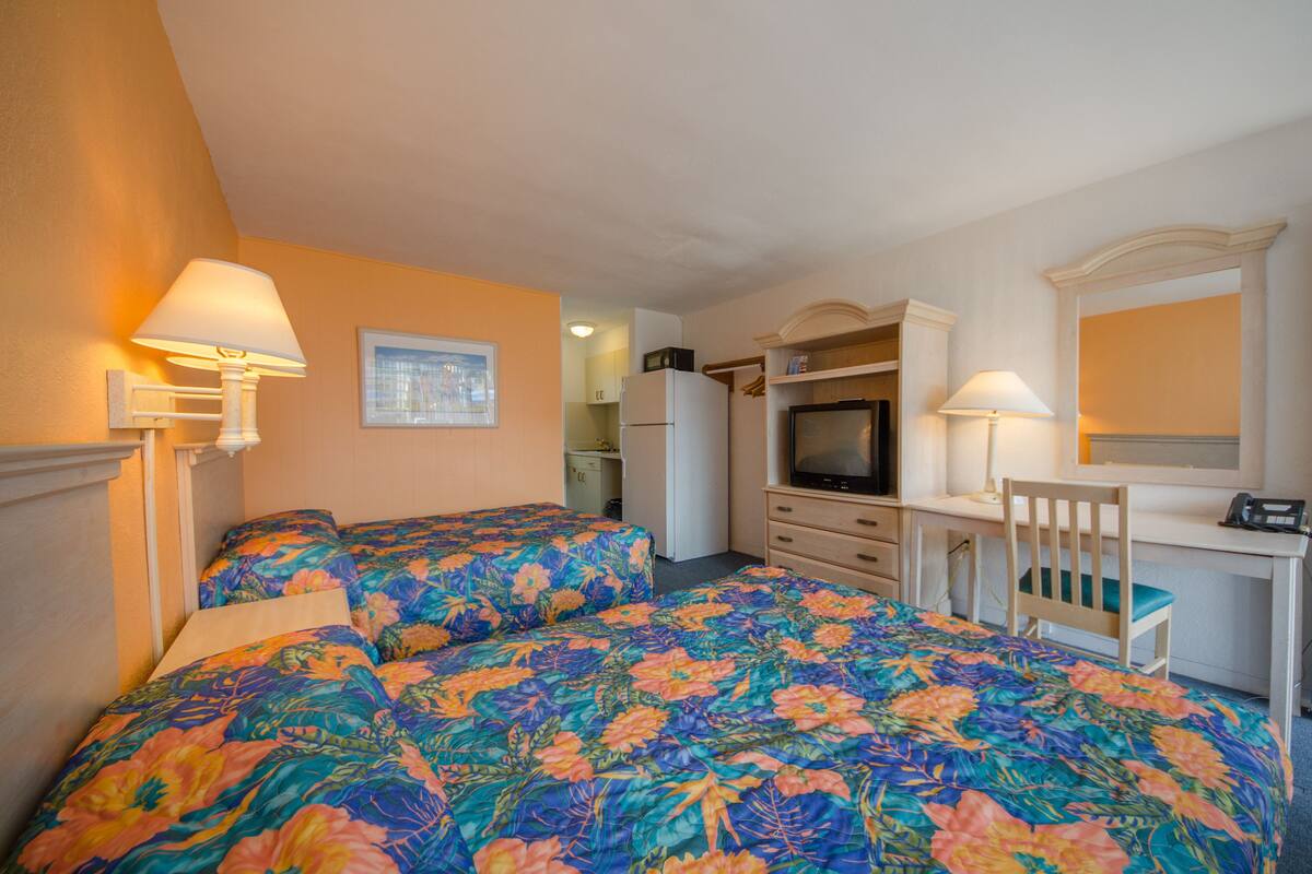 A hotel room with two beds, a desk, a chair, a television, and a refrigerator.