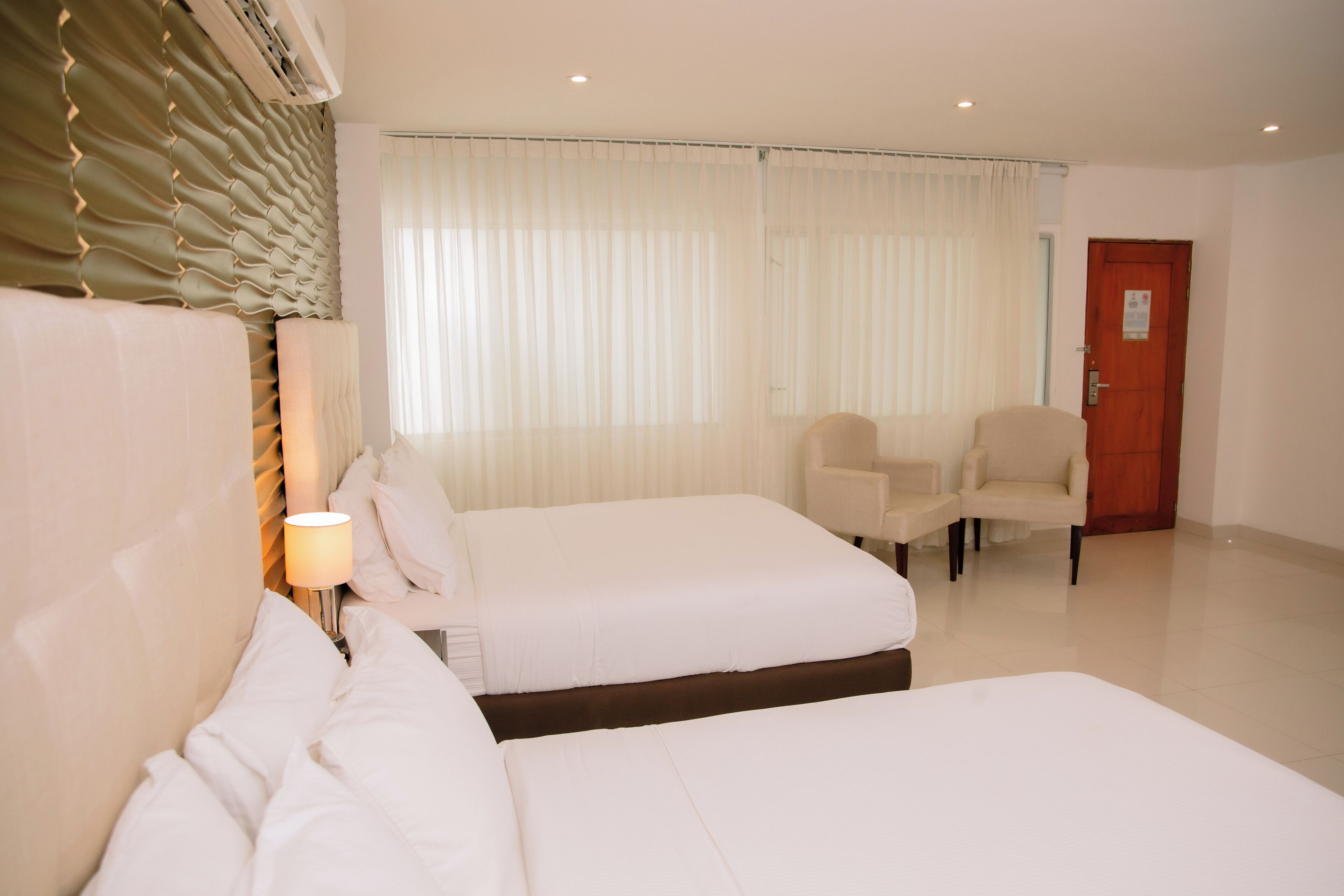 Een hotelkamer met twee bedden, een stoel en een deur.