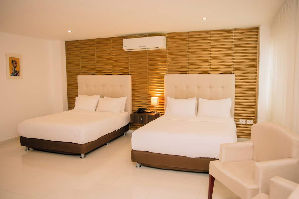 Habitación de hotel con dos camas, una mesita de noche, una silla y un aire acondicionado de pared.