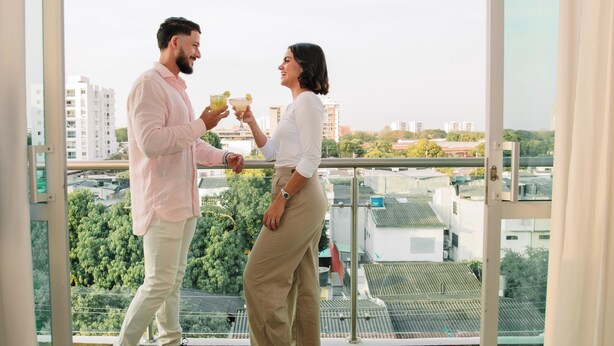 A couple on a balcony with a city view, holding drinks. - Hotel Parque Del Sol (Montería)