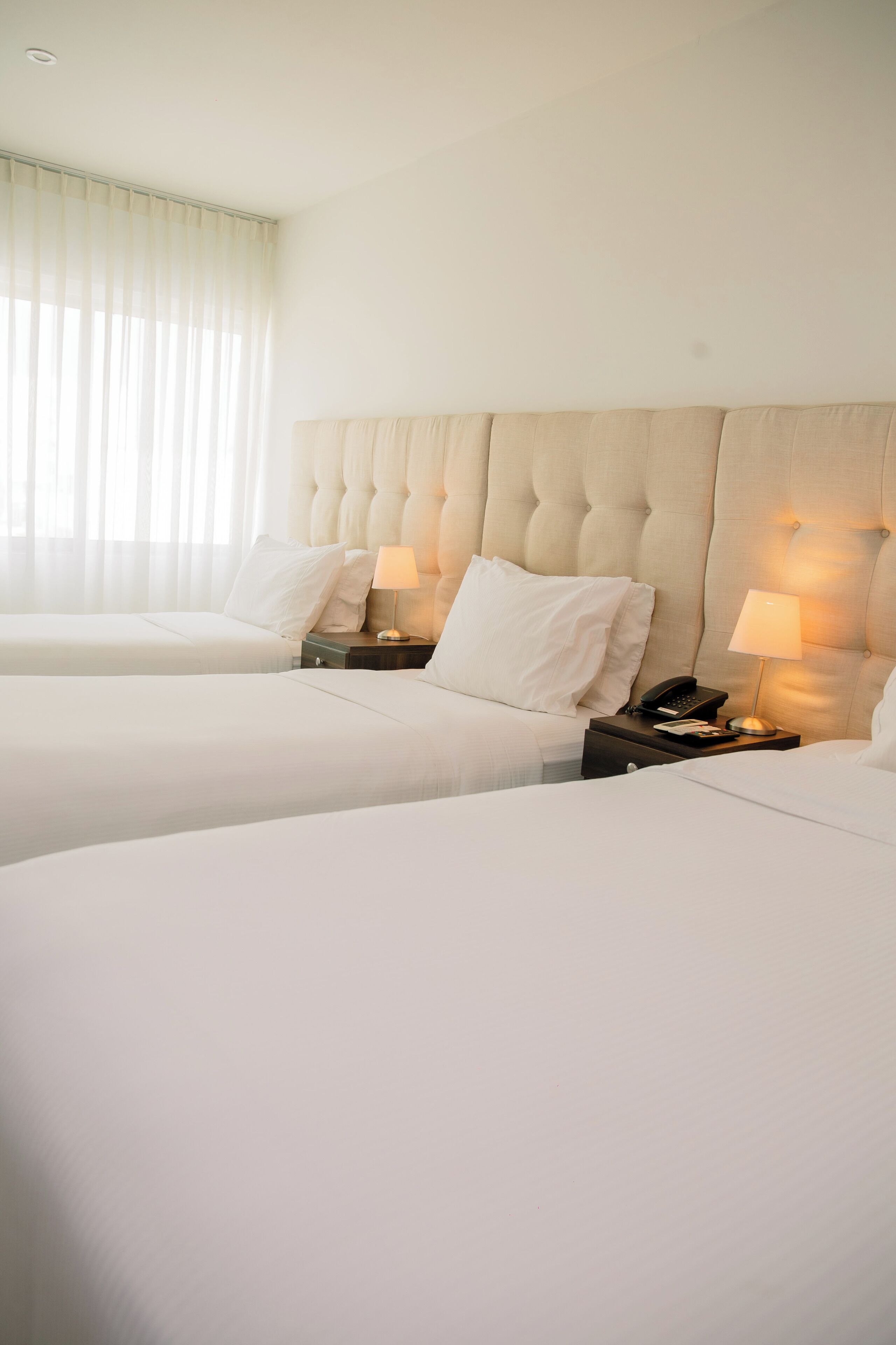 A hotel room with two beds, each with a headboard, bedside tables, and lamps.