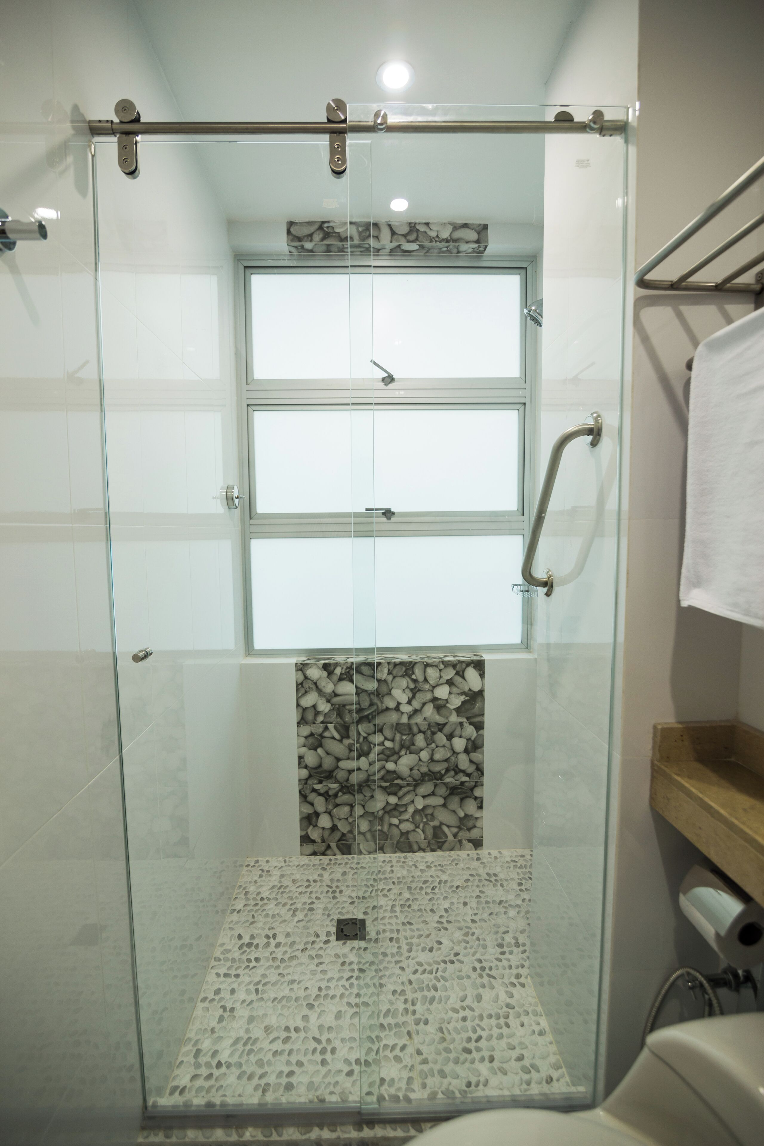 A glass-enclosed shower with a handrail, a tiled floor, and a stone accent wall.