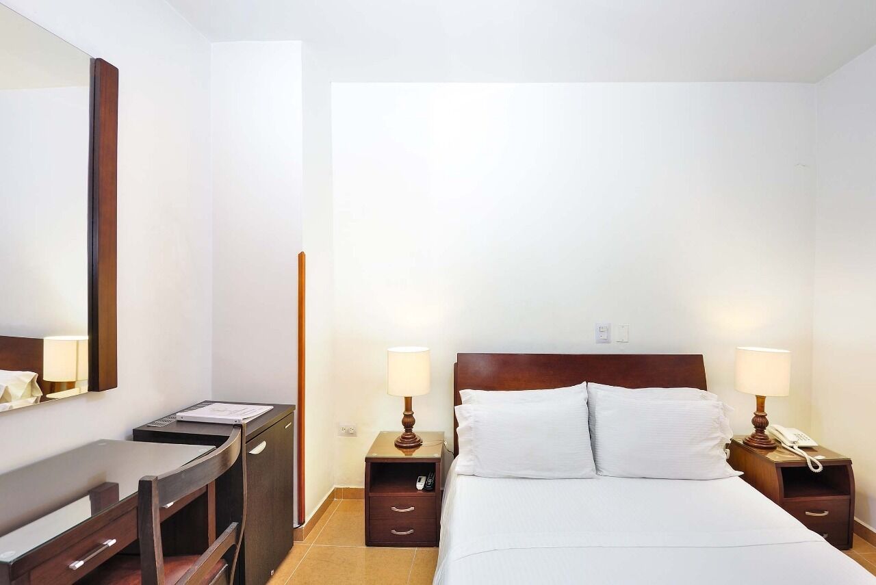 A hotel room with a bed, two bedside tables, a desk, and a chair.