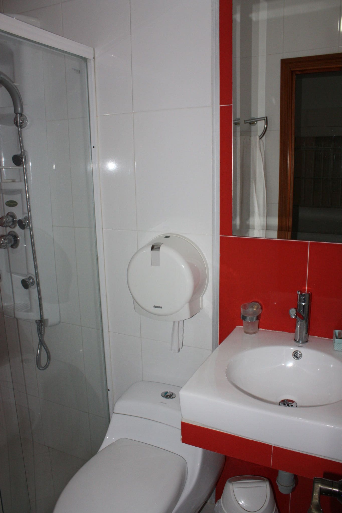 Un bagno con doccia vetro, un water e un lavandino con un dettaglio rosso.
