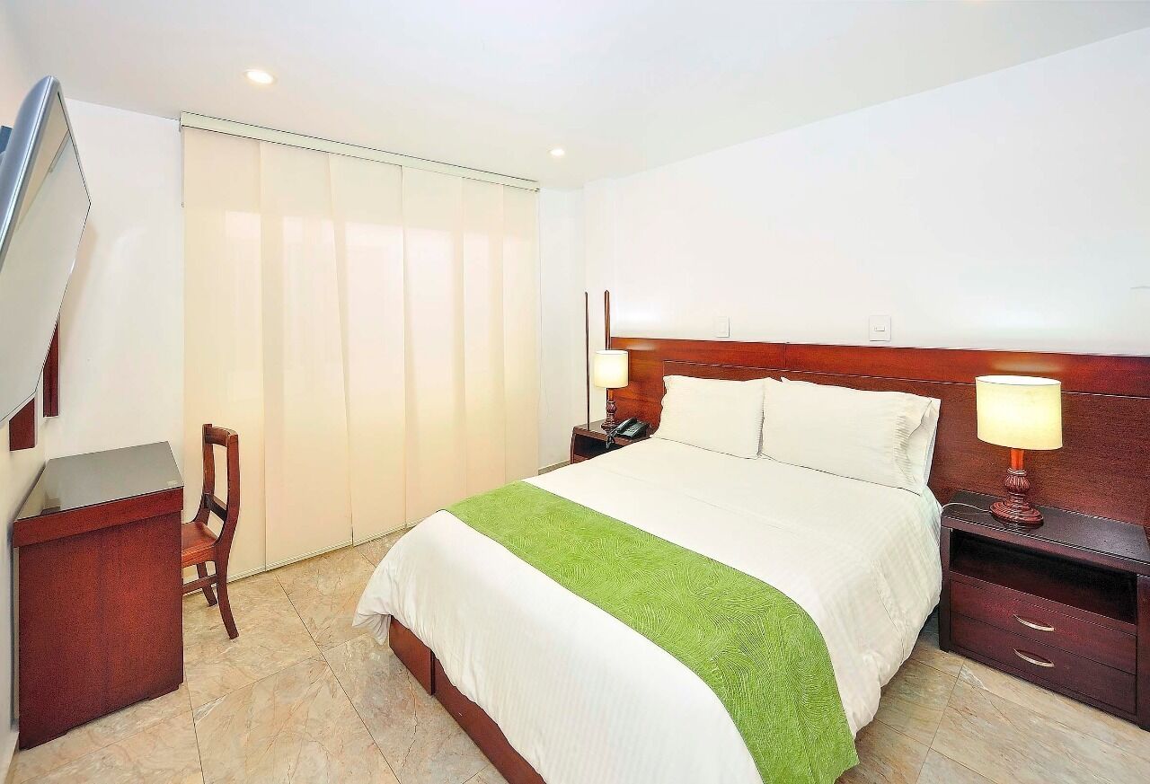 A hotel room with a bed, bedside lamps, a desk, and a chair.