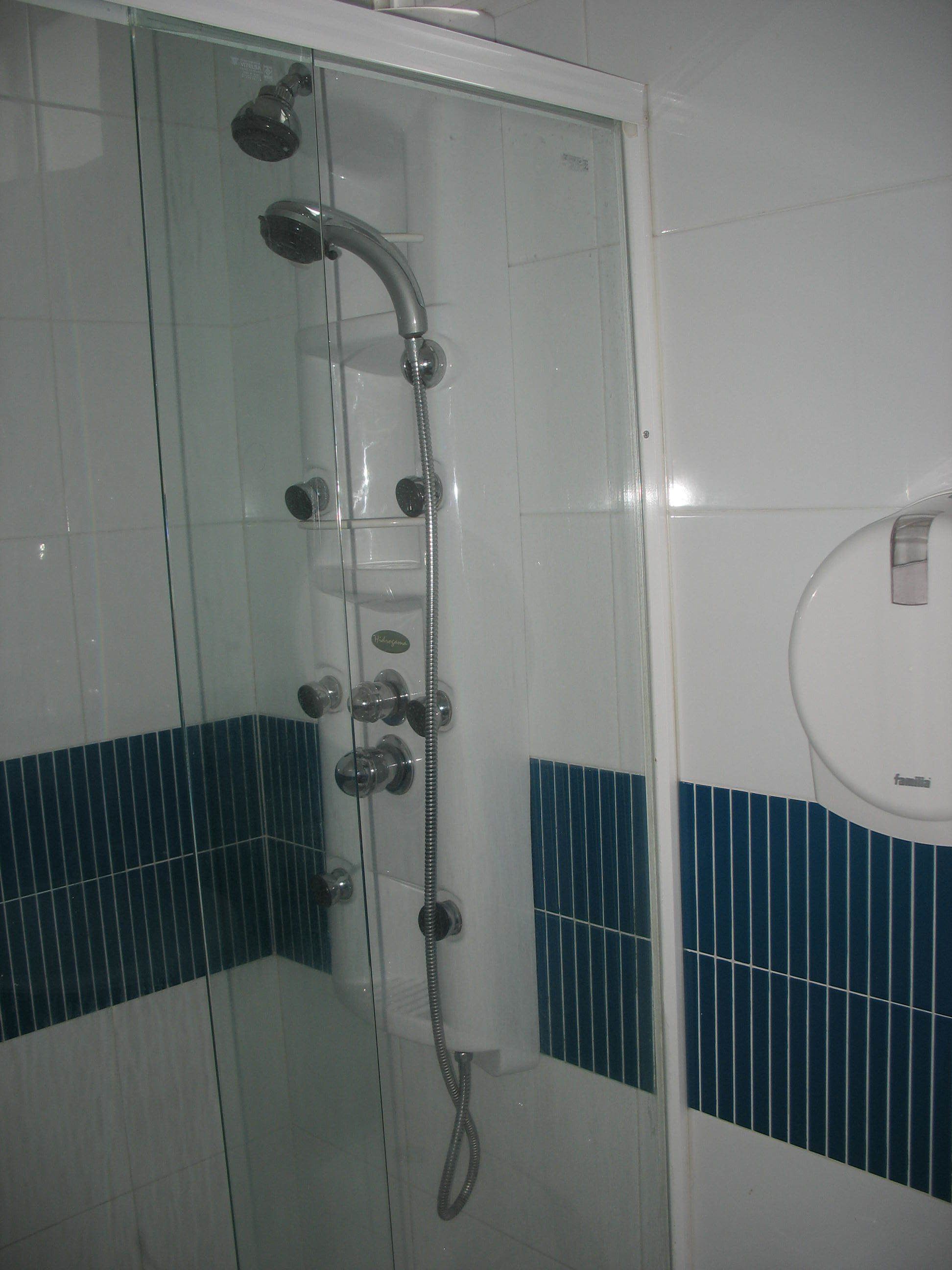 A glass-enclosed shower with multiple controls and a handheld showerhead.