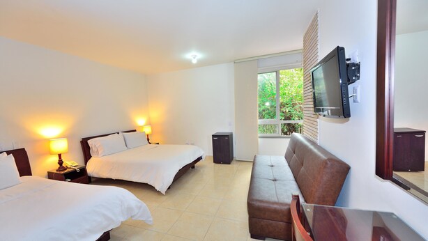 Habitación de hotel con dos camas, un televisor montado en la pared, un sofá y un escritorio.