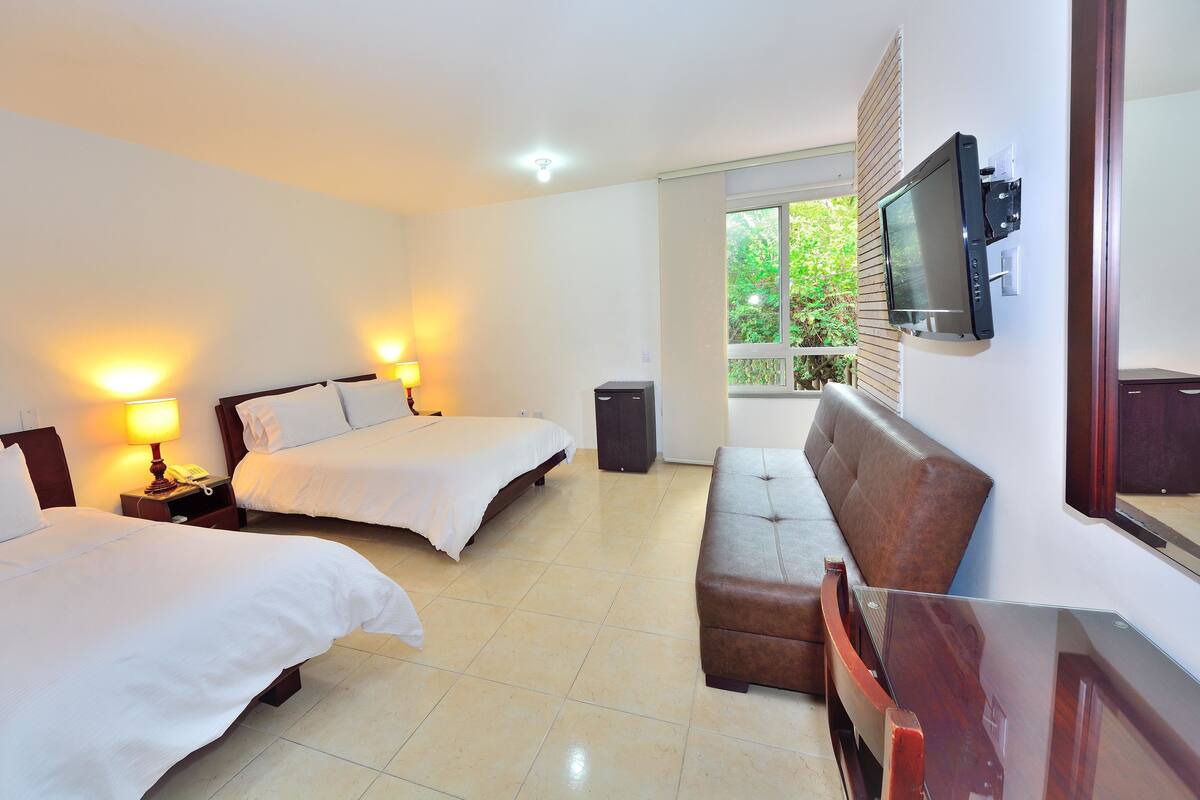 A hotel room with two beds, a TV mounted on the wall, a sofa, and a desk.