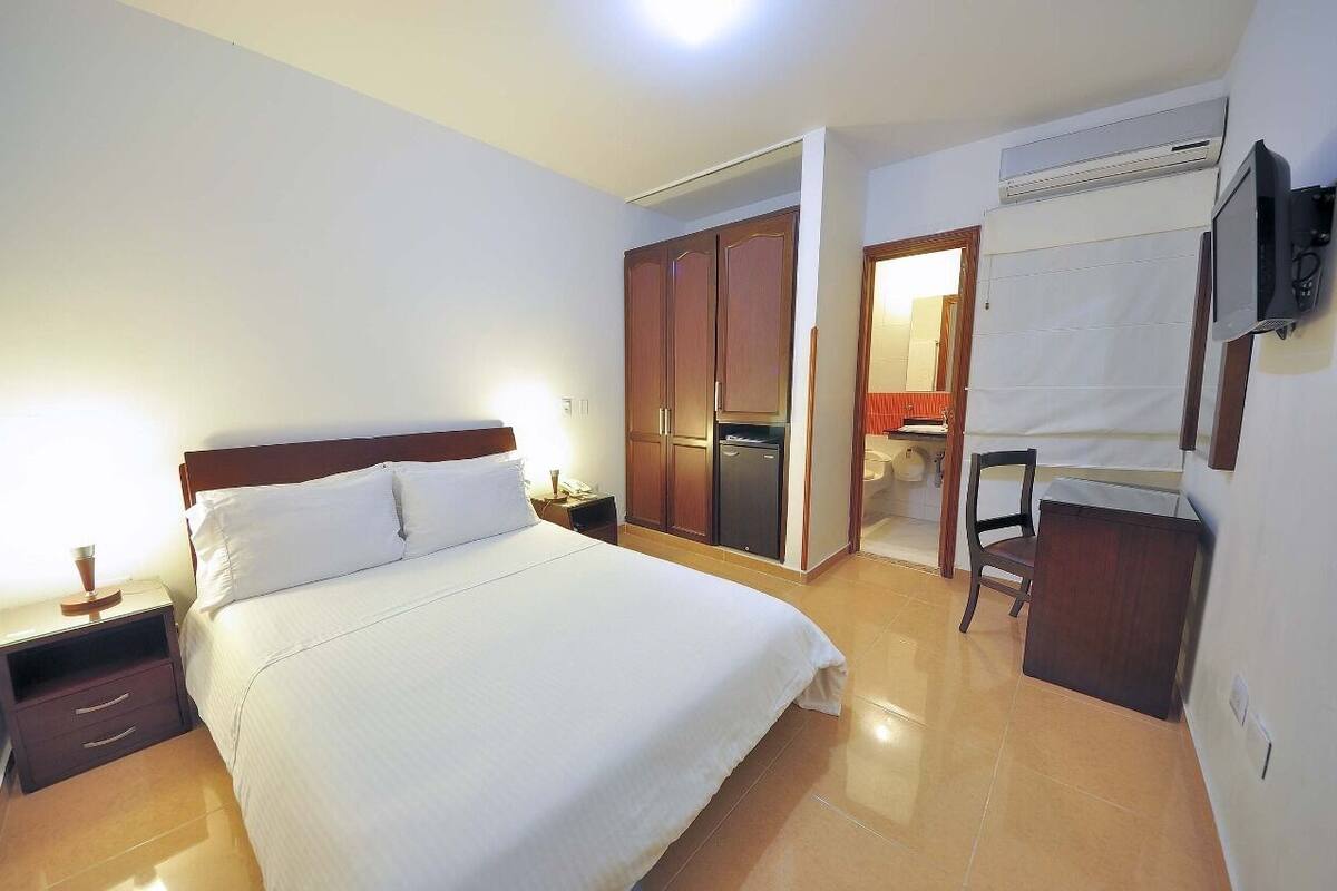 A hotel room with a bed, a nightstand, a wardrobe, a television, and an air conditioning unit.