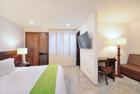 Habitació d'hotel amb un llit, una taula de treball, una cadira, un sofà, un televisor i una làmpada.