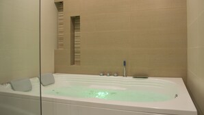 Un baño con bañera, cabina de ducha de vidrio y paredes de cerámica color crema.