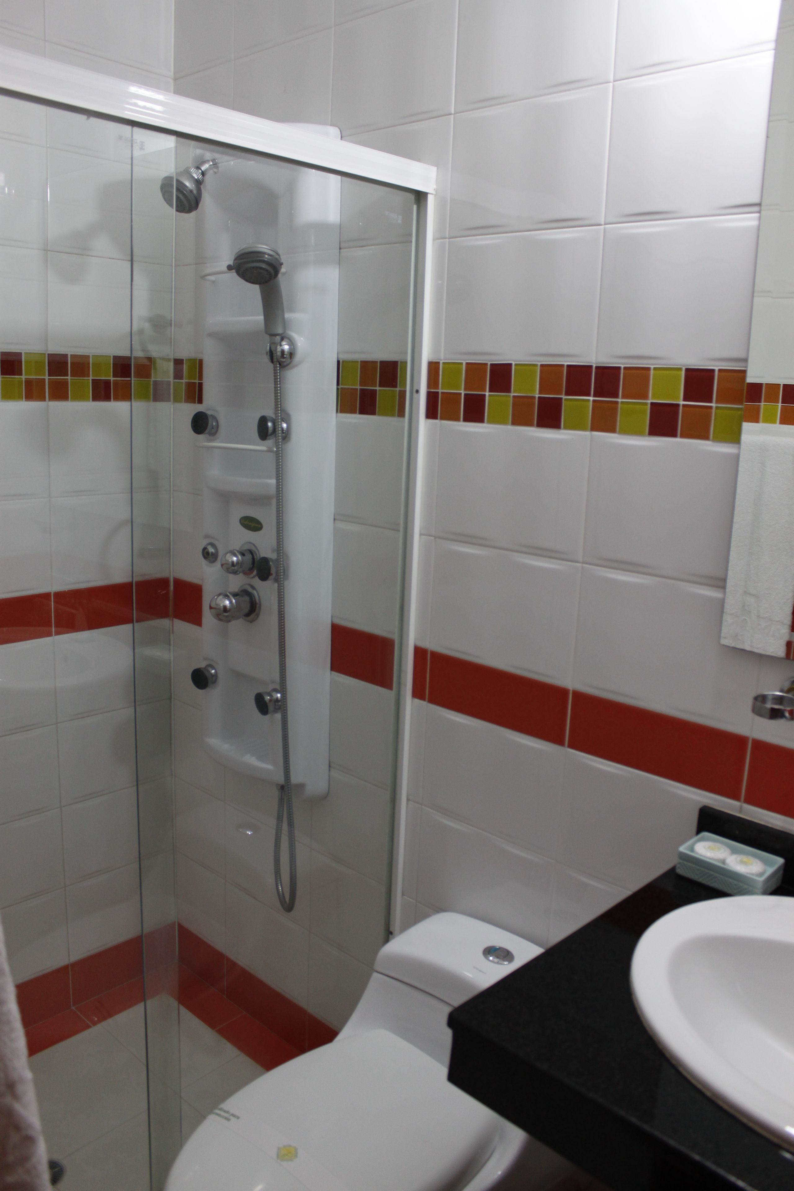 Un baño con ducha de vidrio, inodoro blanco y lavamanos negro sobre encimera blanca.