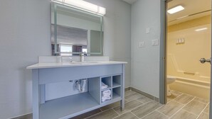 A bathroom with a white sink, mirror, and shelves. There is a shower visible through an open door. - Americas Best Value Inn Stearns (Stearns)