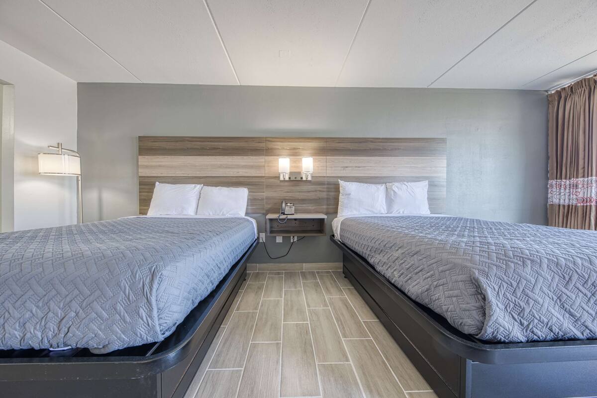 A hotel room with two beds, a nightstand with two wall-mounted lamps, and a wooden headboard.
