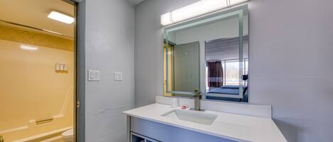 Un baño con lavamanos blanco, un espejo y un perchero para toallas.