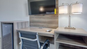 A hotel room with a wooden desk, a flat-screen TV, a desk lamp, a chair, and a mini-fridge. - Americas Best Value Inn Stearns (Stearns)