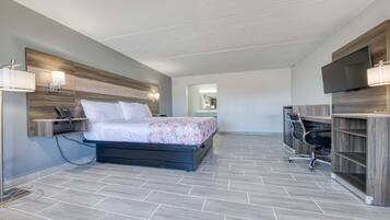 Une chambre d’hôtel moderne équipée d’un lit, de lampes de chevet, d’un bureau avec une chaise et d’un téléviseur à écran plat fixé au mur.