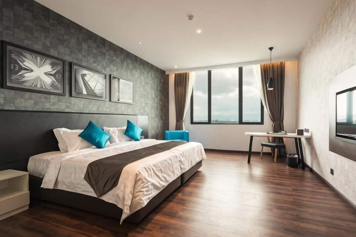 A modern hotel room with a large bed, a desk, and a view of the city.
