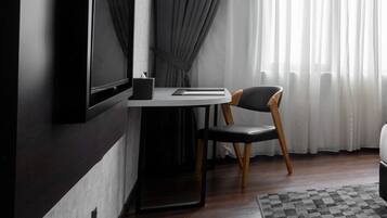 A modern room with a flat-screen TV mounted on a dark wall, a small white table with a chair, and a patterned rug on the wooden floor.