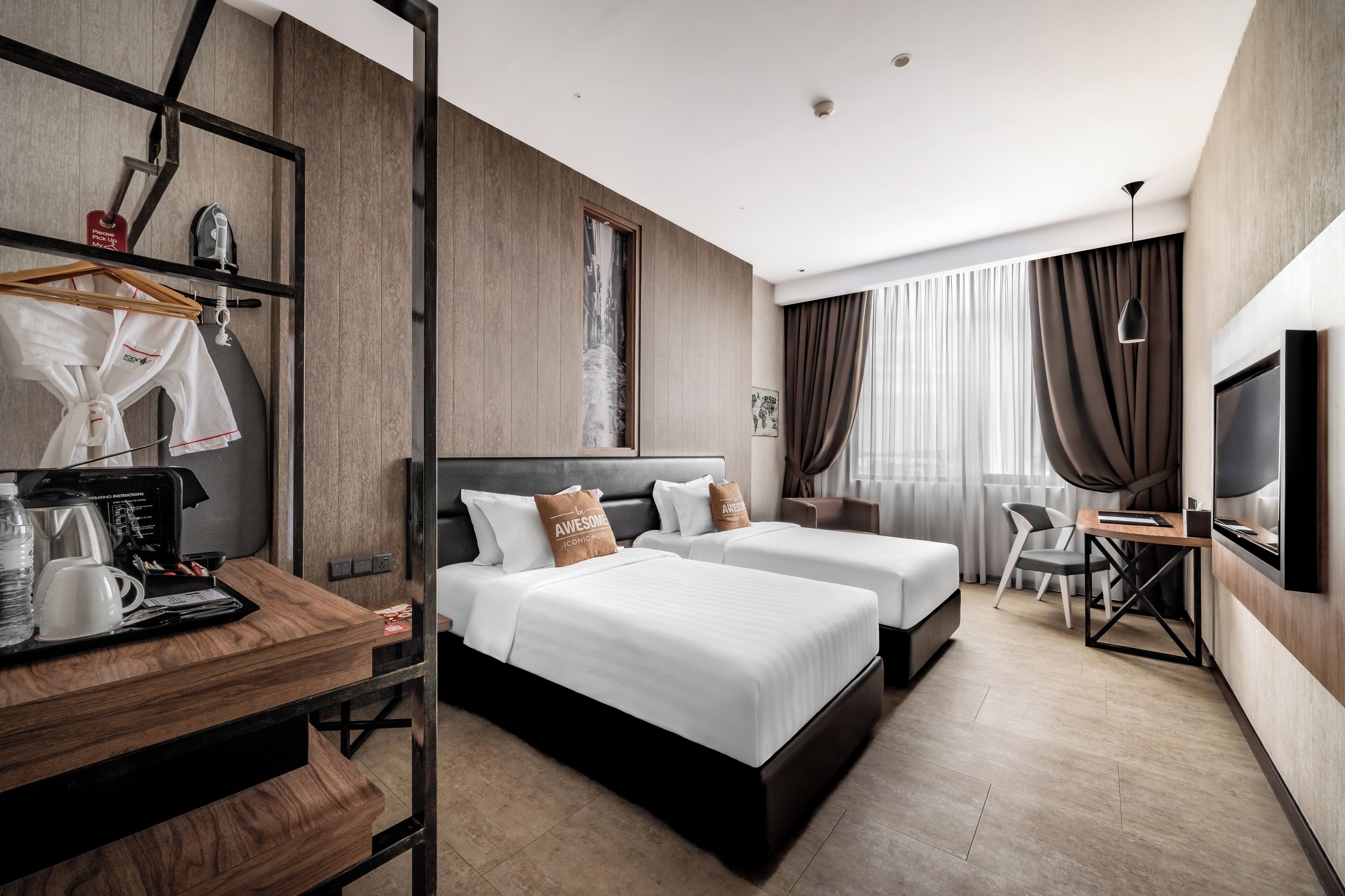 A modern hotel room with two beds, a desk with a coffee maker, a TV, and a wardrobe.