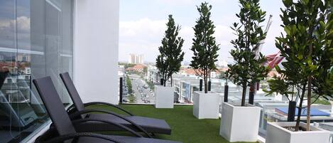 A balcony with artificial grass, two lounge chairs, and potted trees.