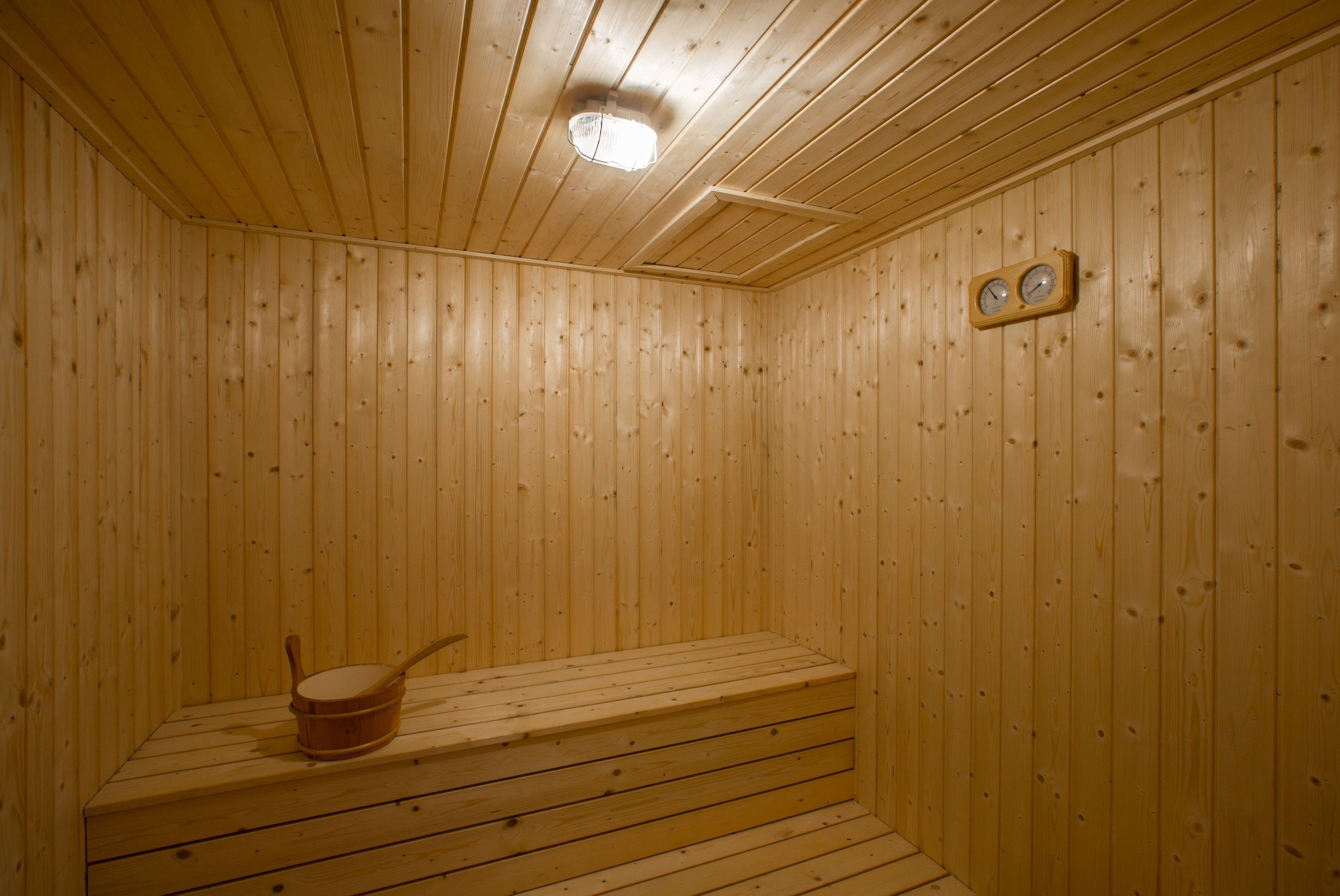 Een houten sauna met een bank, een kachel en een klok aan de muur.