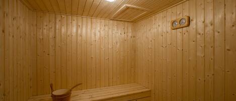 A wooden sauna room with a bench, a heater, and a wall-mounted clock.