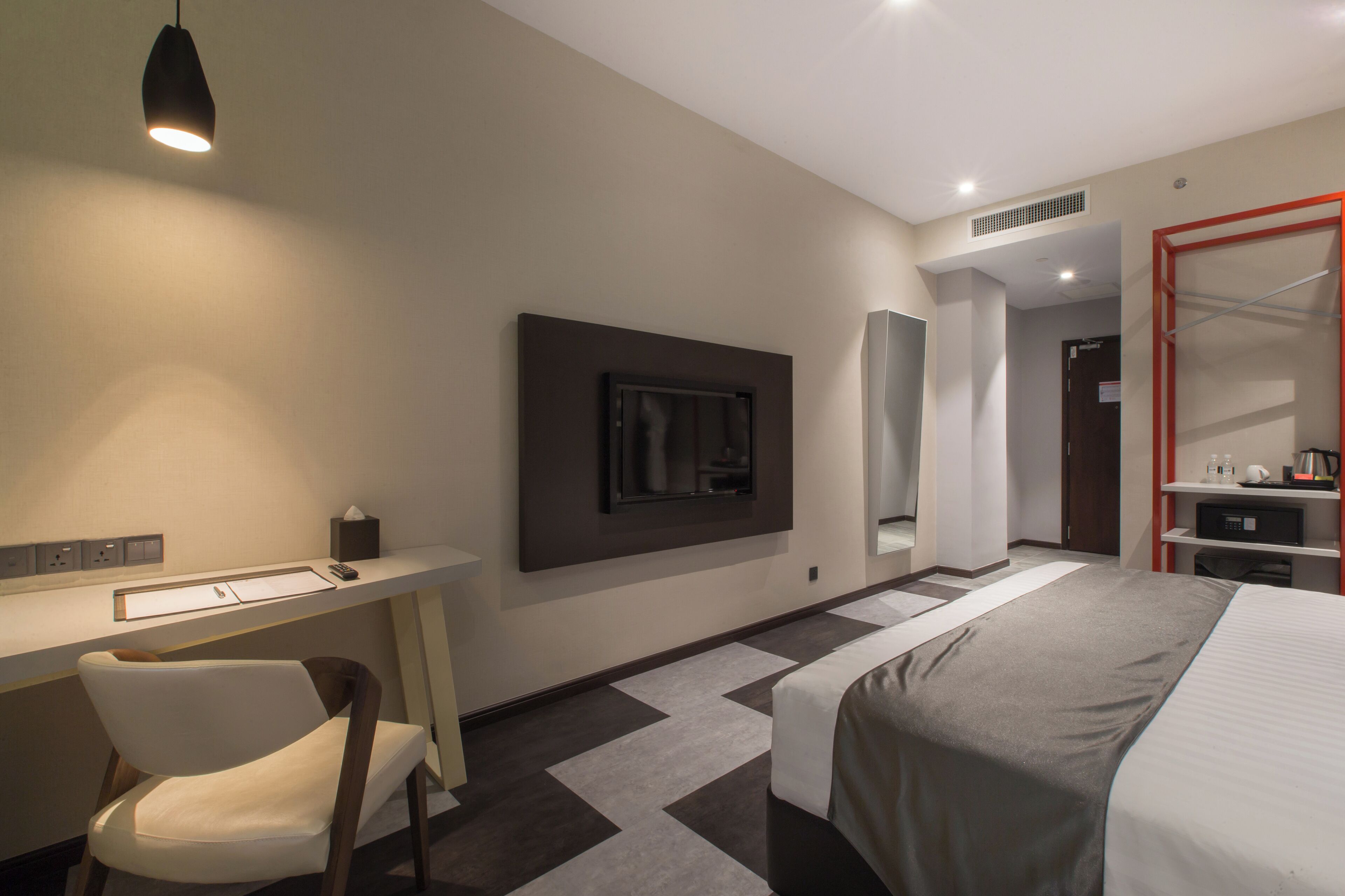 A modern hotel room with a bed, desk, chair, and a television mounted on the wall.