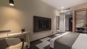 A modern hotel room with a bed, desk, chair, and a television mounted on the wall.