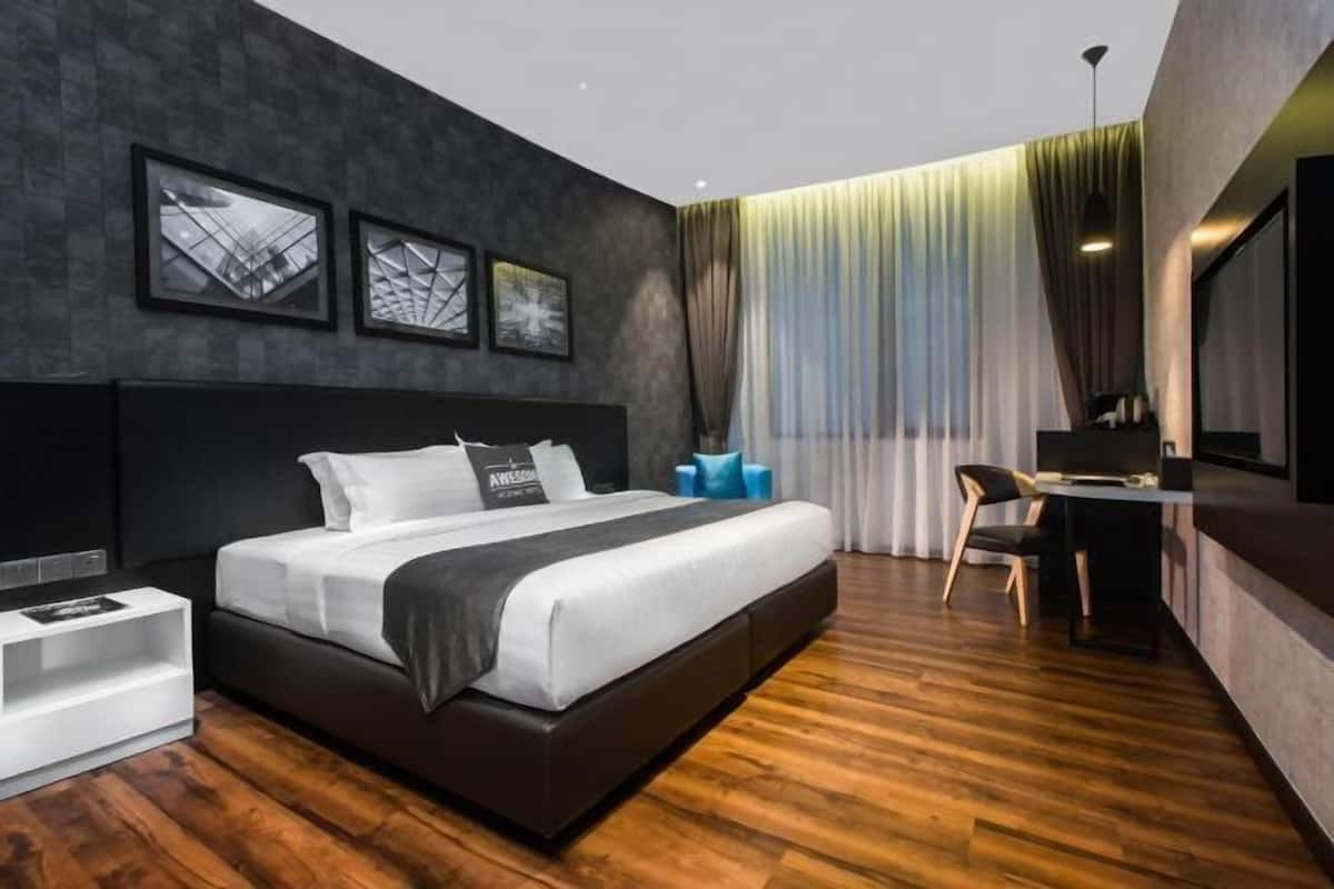 A modern hotel room with a large bed, a desk, and a view of the cityscape through the window.