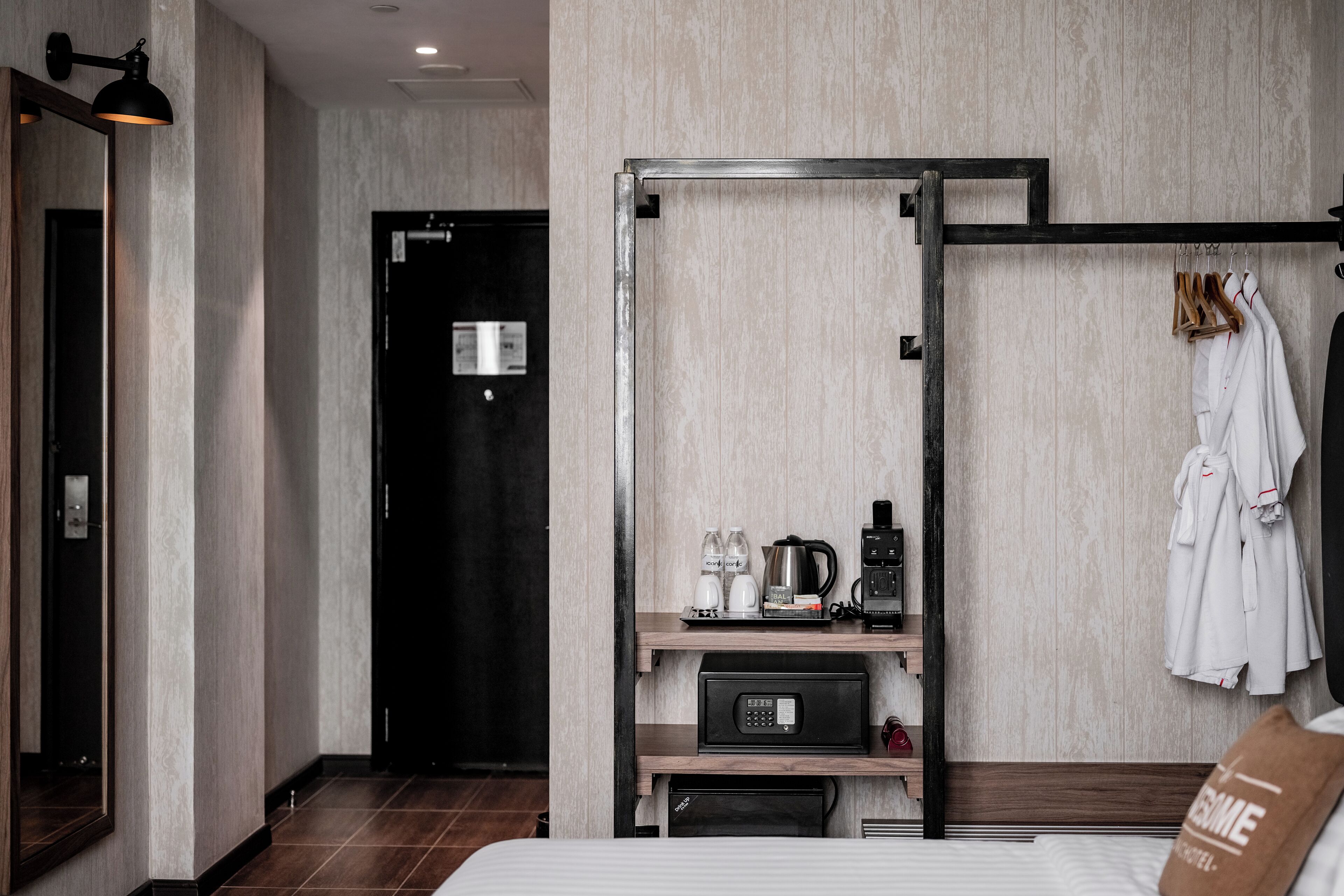 Een moderne hotelkamer met een bed, een kledingkast, een plank met toiletartikelen, een koffiezetapparaat en een telefoon.