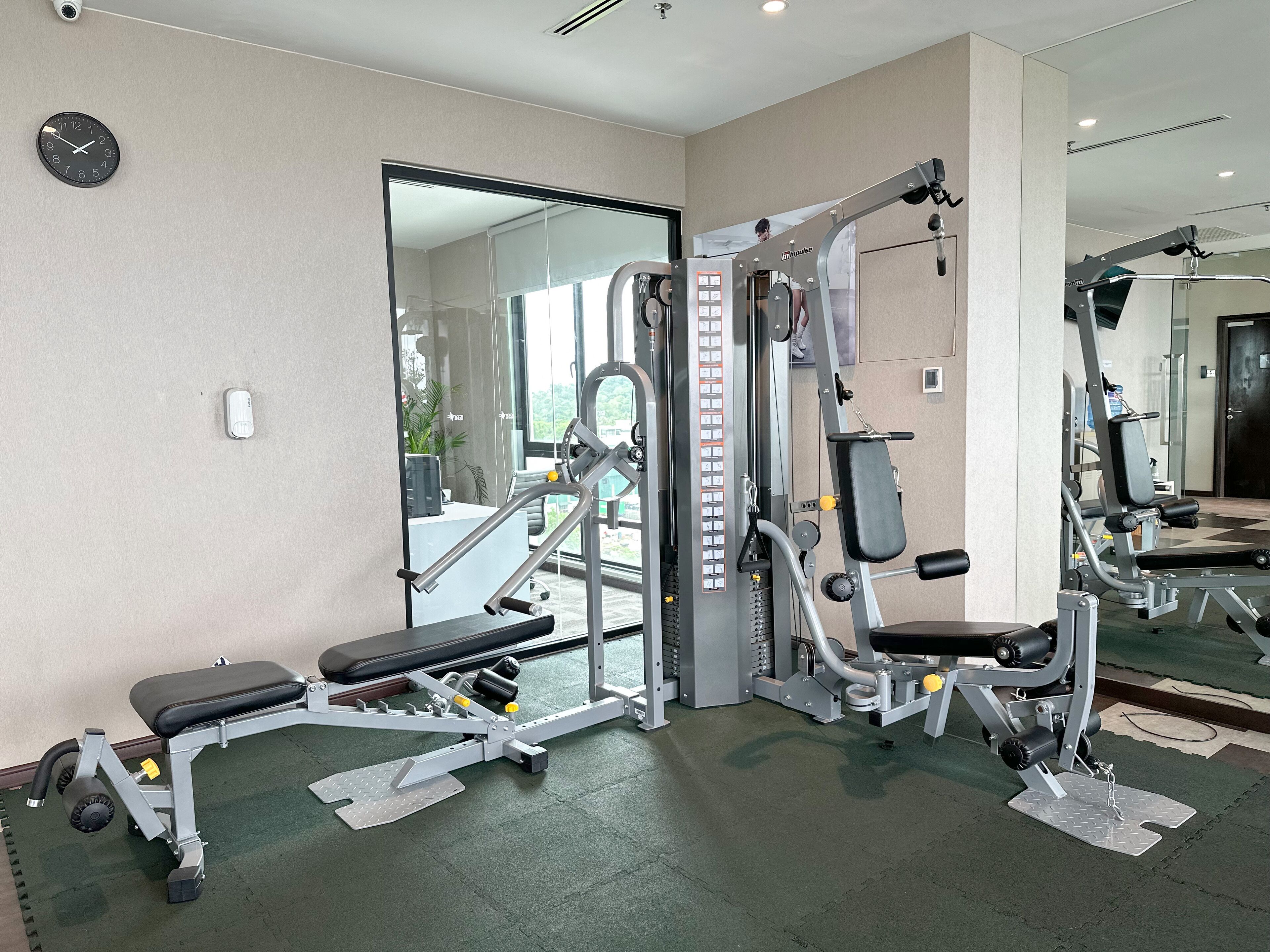 Une salle de sport équipée de divers appareils d’exercice, d’une horloge et d’un grand miroir.