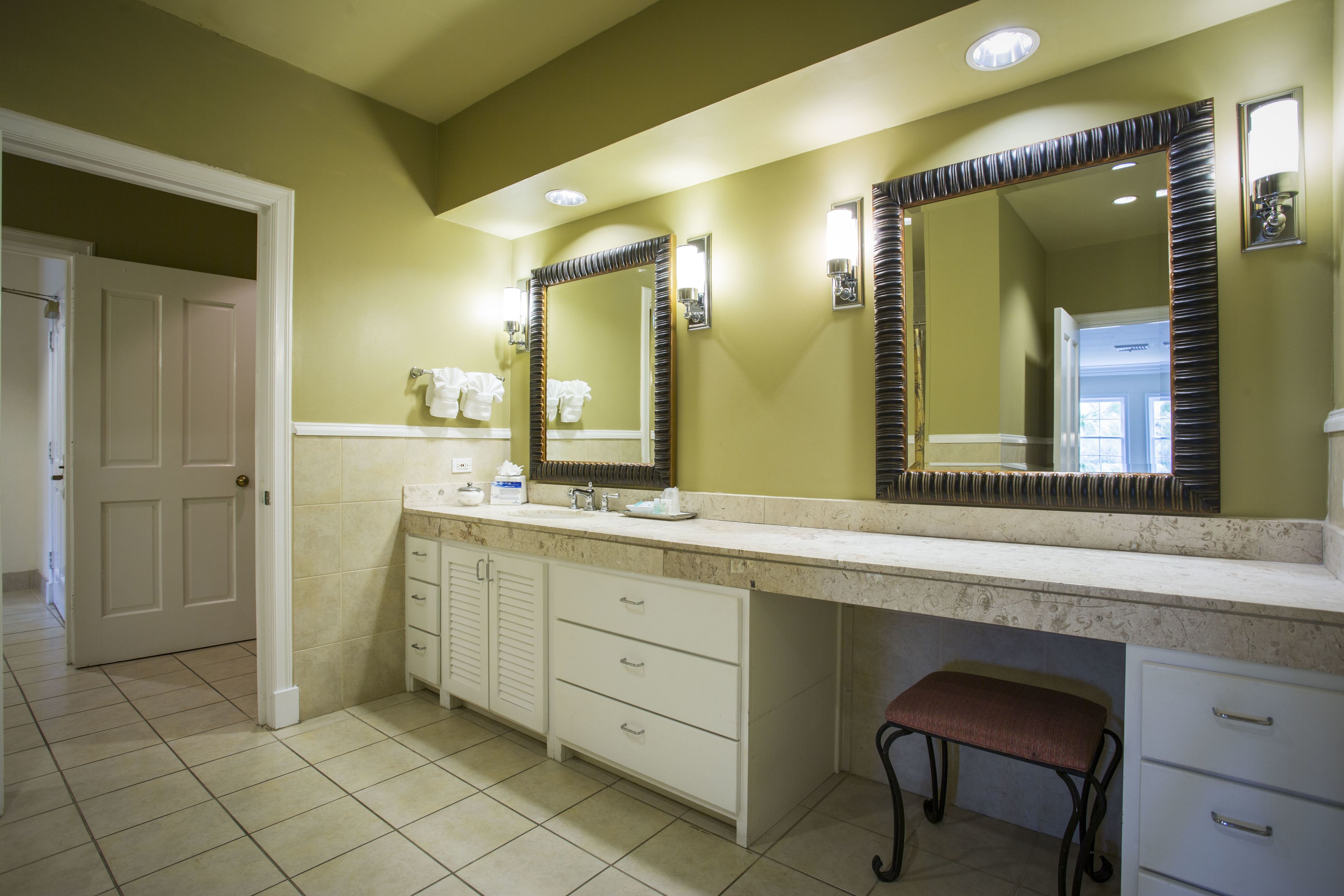 Une salle de bain dotée d’un grand meuble-lavabo, d’un banc et de deux miroirs.
