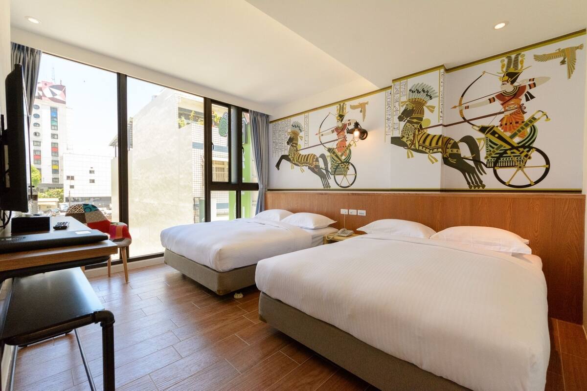 Une chambre d’hôtel avec deux lits, un bureau et une grande fenêtre.