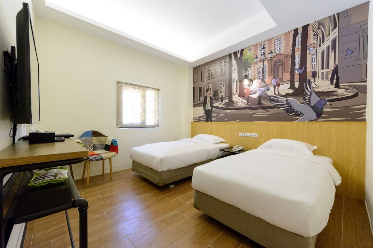 Une chambre d’hôtel avec deux lits, un bureau, une chaise, un téléviseur et une fresque murale.