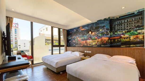 Quarto de hotel com duas camas, uma escrivaninha e uma janela grande com vista para a cidade.