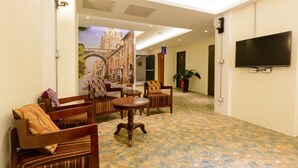 Um saguão com móveis de madeira, uma mesa redonda, uma televisão e um mural de um edifício histórico.