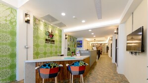 Uma área de recepção com parede estampada em verde, um balcão de atendimento e dois taboretes coloridos.
