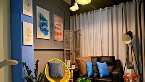 Una sala de estar acogedora con un sofá, un sillón amarillo y una mesa de centro. Hay cuadros enmarcados en la pared y una lámpara al lado.