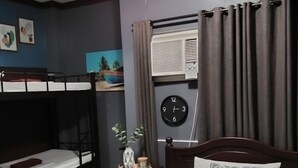 Habitación de hotel con una cama individual, una cama nido más pequeña, una mesita de noche con un reloj y un equipo de aire acondicionado.