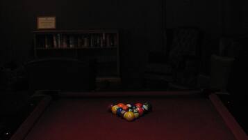 A billiards table with balls and a cue stick, a bookshelf, and a stained glass lamp.
