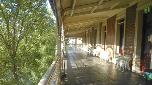 A covered outdoor area with a wooden deck, white metal chairs, and tables. - Criterion Hotel Warwick (Warwick)