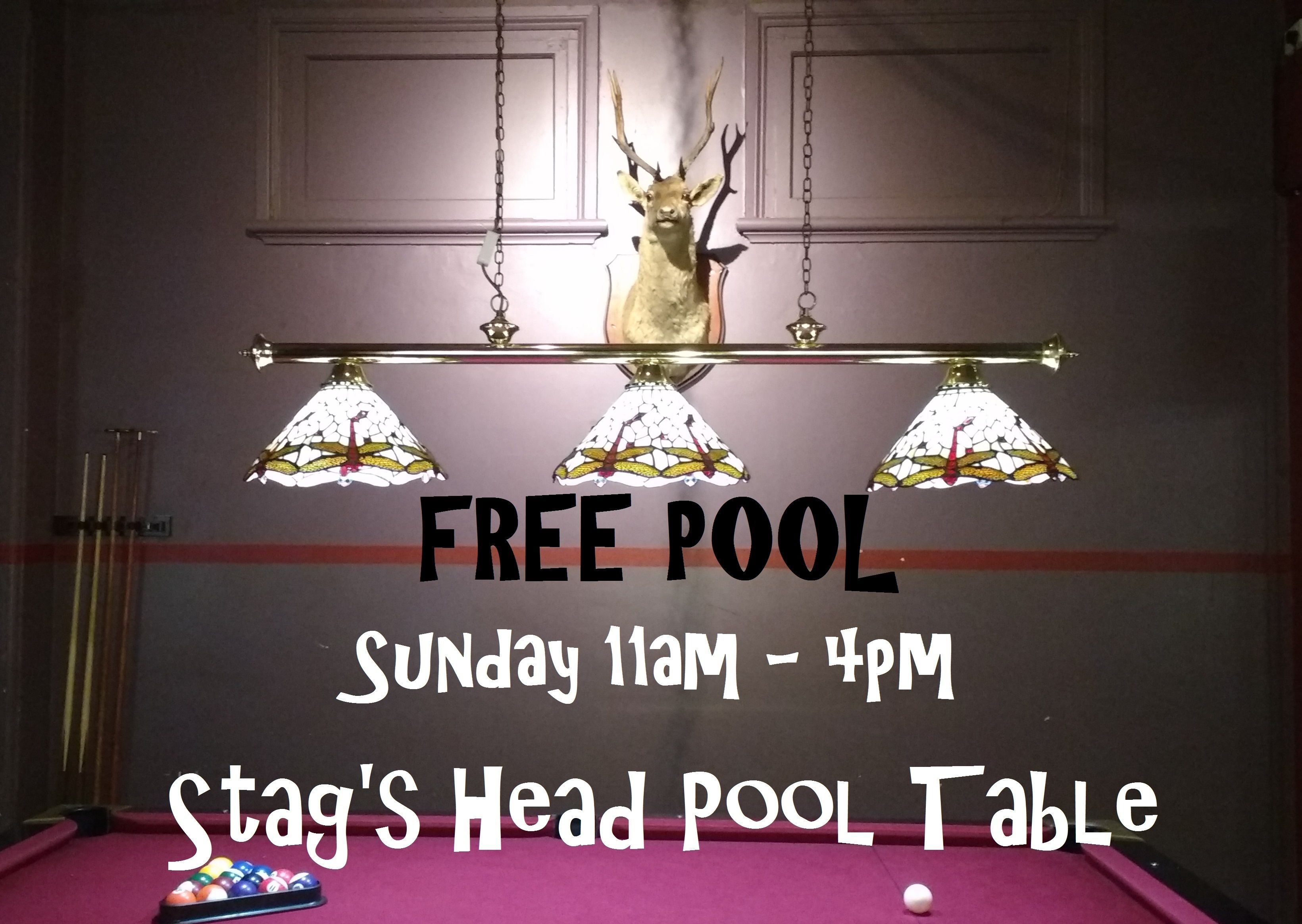 Una mesa de billar con una decoración de cabeza de ciervo colgada encima, y texto que indica acceso gratuito al billar los domingos de 11 de la mañana a 4 de la tarde en Stag's Head Pool Table.