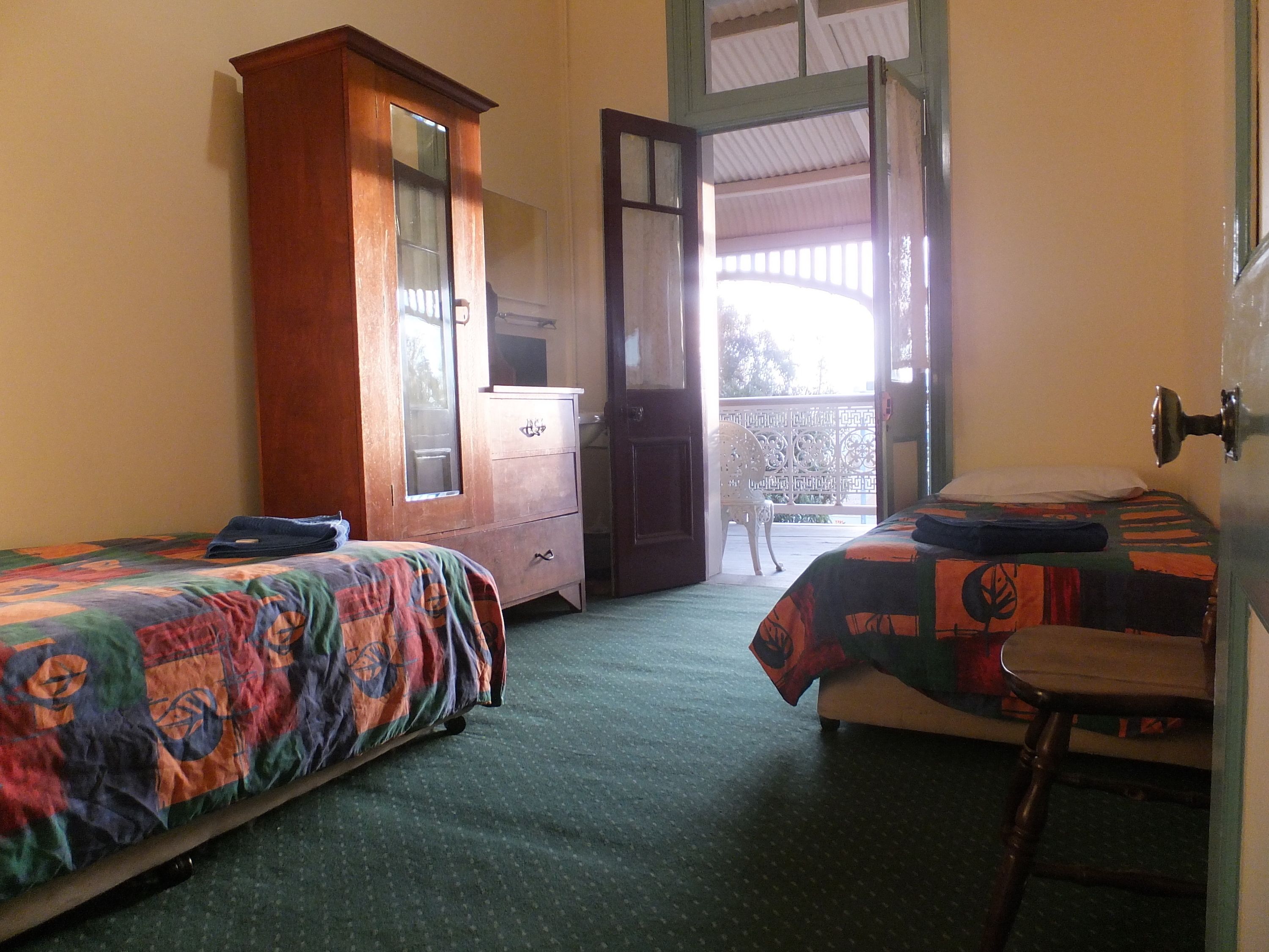 A room with two beds, a wooden wardrobe, a chair, and a balcony with a view.