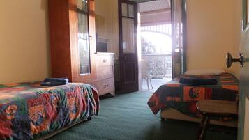 A room with two beds, a wooden wardrobe, a chair, and a balcony with a view.