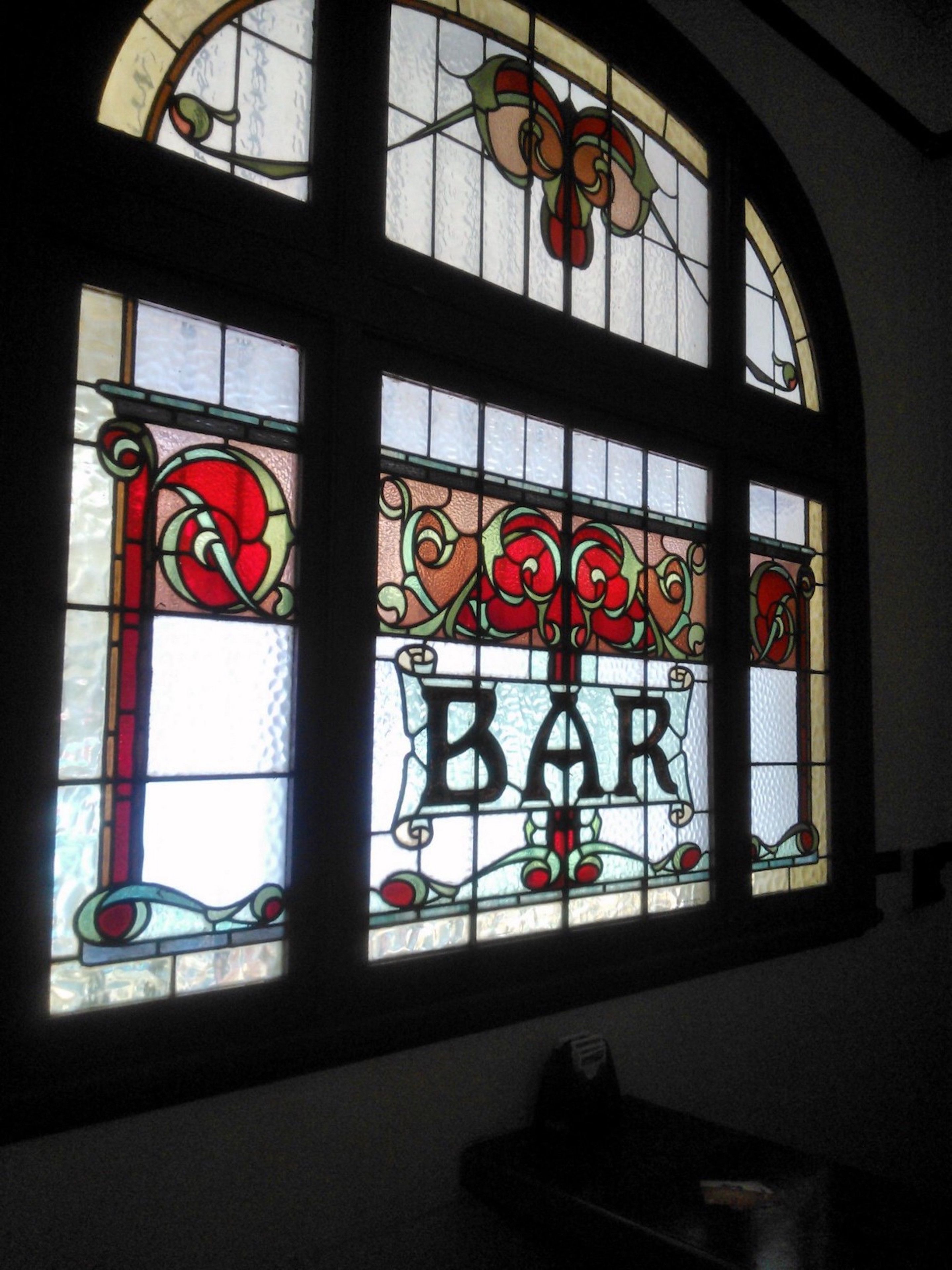 Una vidriera con la palabra "BAR" en el centro, rodeada de motivos florales decorativos.