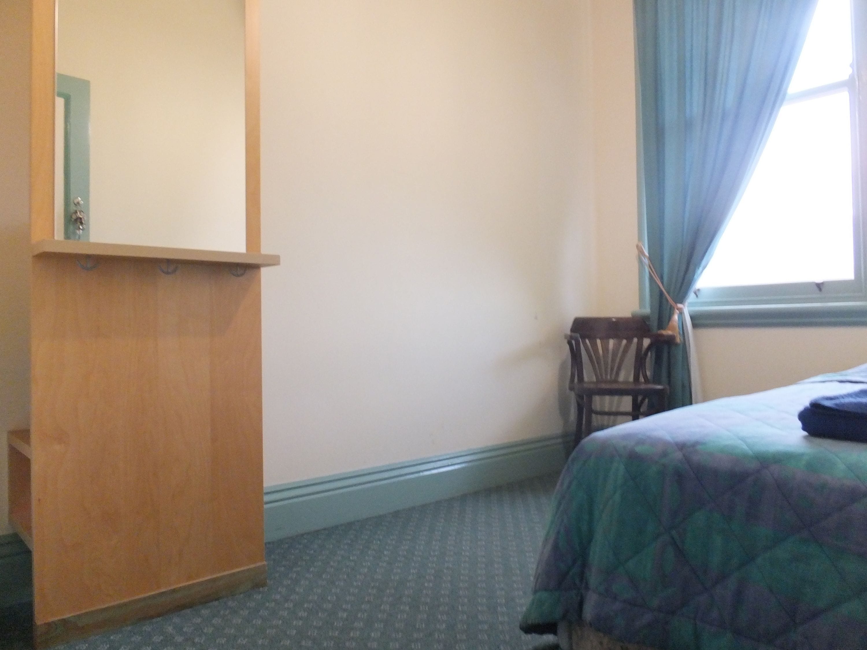 A room with a wooden desk, a bed with a quilt, a chair, and a window with curtains.