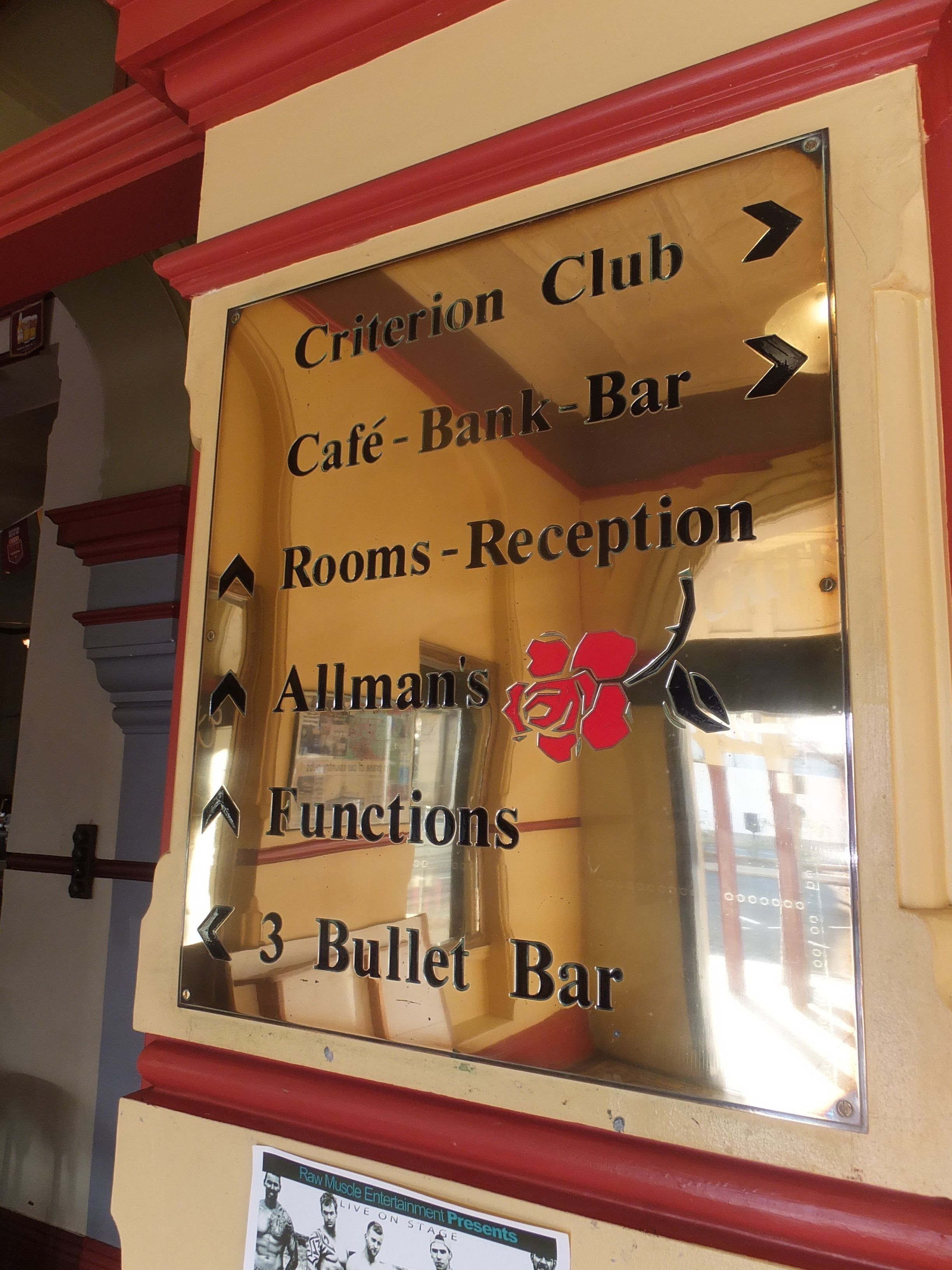 Ein Hinweisschild mit Pfeilen, die zu verschiedenen Orten zeigen, wie Criterion Club, Café – Bank – Bar, Zimmer – Rezeption, Allman's Functions und 3 Bullet Bar.