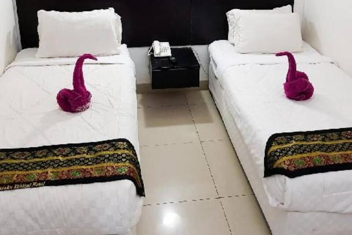 A hotel room with two beds, white bedding, a black headboard, a nightstand with a phone, and two framed pictures on the wall.