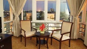 A room with a balcony, two chairs, a small table with a vase, and a view of the cityscape at dusk. - Green Leaf Hotel (Yangon)